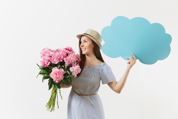 Young woman in blue dress, hat holding blank empty say cloud, speech bubble with place text, bouquet of pink peonies flowers isolated on white background. Holiday concept. Advertising area copy space.