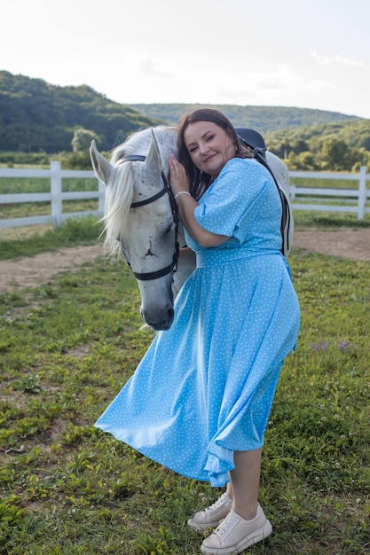 Young woman in a blue dress with horse at the farm