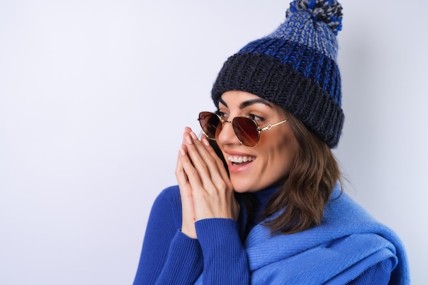 Young woman in a blue golf turtleneck hat and scarf sunglasses on a white background cheerful in a good mood