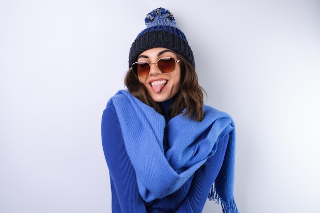 Young woman in a blue golf turtleneck hat and scarf sunglasses on a white background cheerful in a good mood