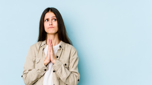 Young woman on blue holding hands in pray near mouth, feels confident.