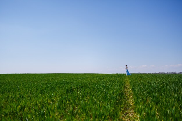 Young woman in a blue long dress on a background of green field. Fashion portrait of a beautiful girl with a smile on her face