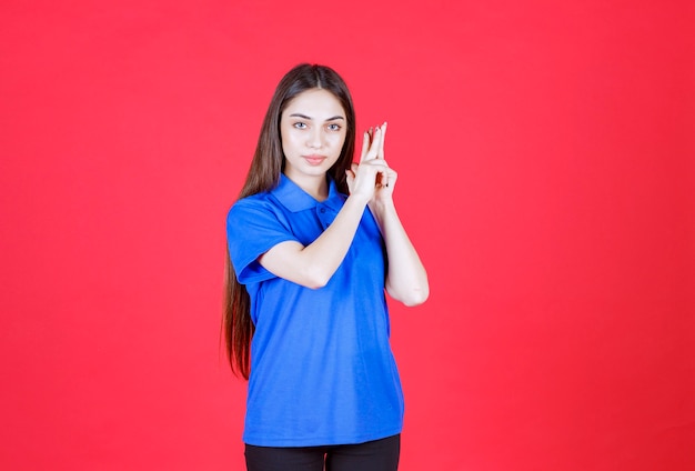 Young woman in blue shirt standing on red wall and looks confused and thoughtful