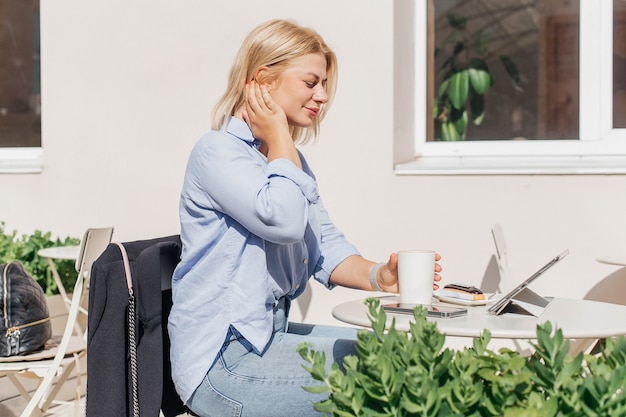 Young woman in a blue shirt working on a notebook in a cafe and drink coffee