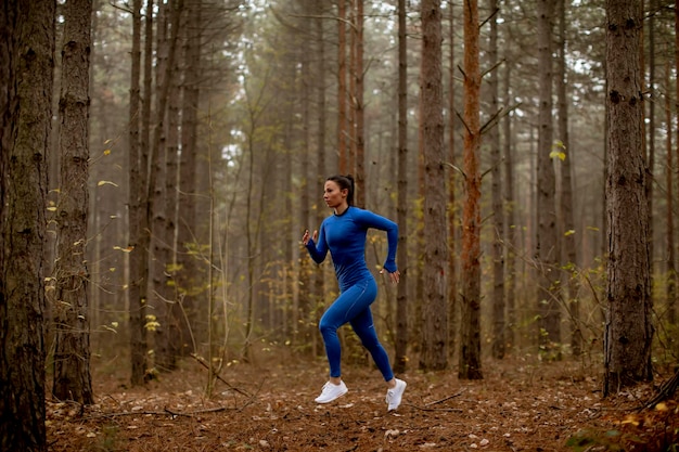 Young woman in blue track suit running on the forest trail at autumn