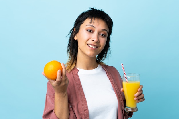 Young woman over blue wall holding an orange and an orange juice