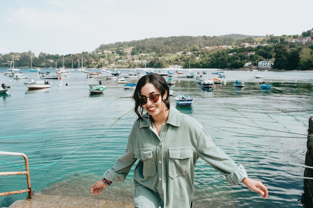 Young woman in a boat dock smiling during a sunny day while using sunglasses beach day