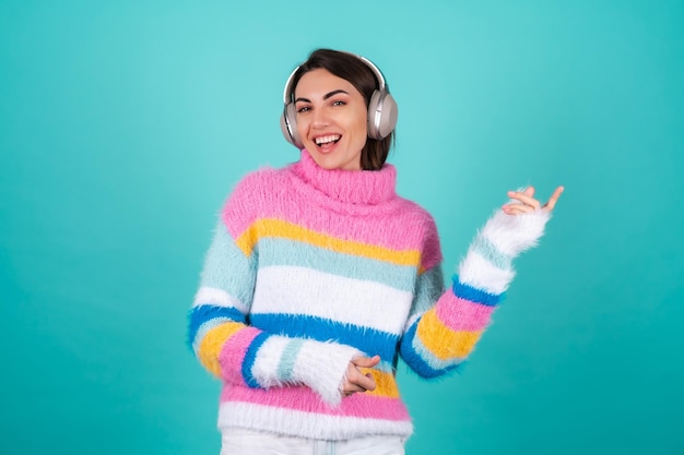 Young woman in a bright multicolored sweater on blue in large noise canceling headphones