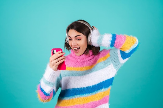 Young woman in a bright multicolored sweater on blue in large noise canceling headphones