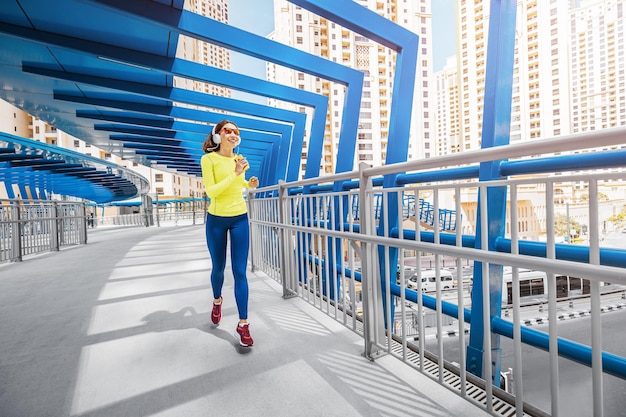 Young woman in bright sportswear quickly runs across a pedestrian bridge in the Dubai Marina district The concept of a female healthy lifestyle and fitness