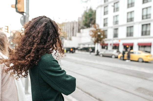 The young woman brunette with curly hair stands on the bus stop