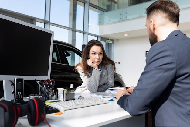 A young woman buyer in a car dealership learns from a consultant the details of a transaction for