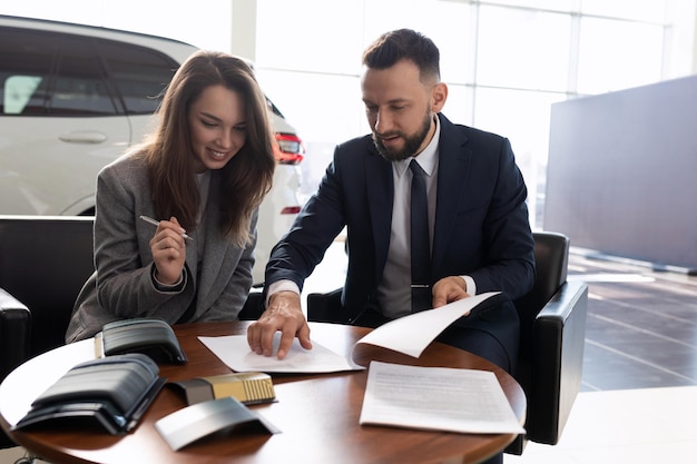 Young woman buys a new car in a car dealership and signs documents car insurance concept