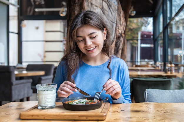 A young woman in a cafe dines on traditional shakshuka and ayran