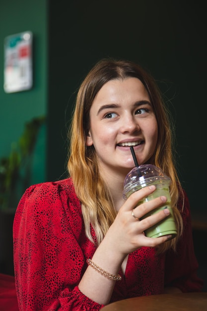 A young woman in a cafe drinks a green drink ice latte