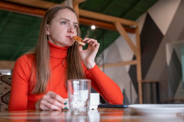 Young woman in cafe is trying snack Girl sits at table in cafe and holds dessert in her hand Pensive or sad woman