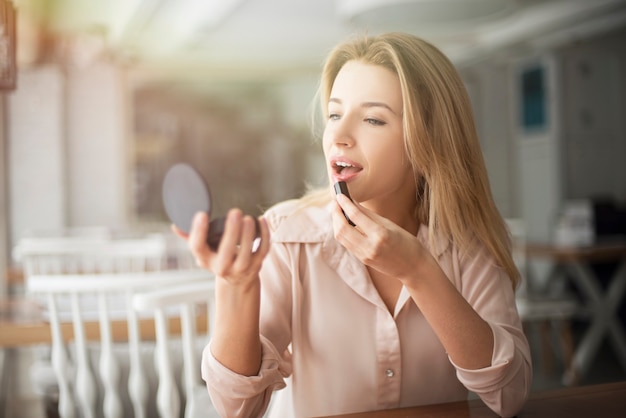 Young woman in cafe sitting applying pomade looking at mirror concentrated