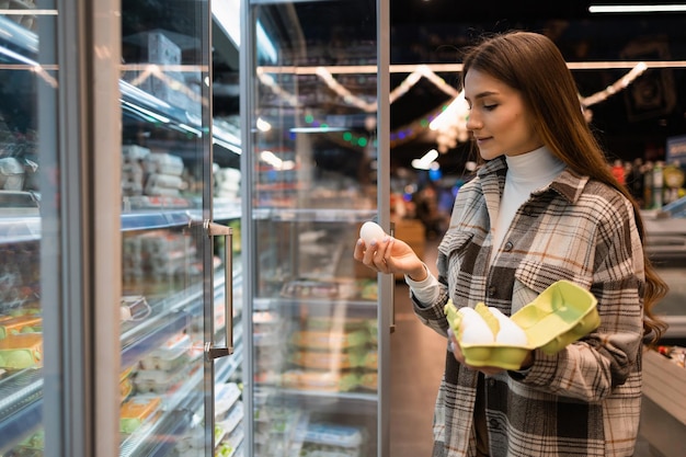 Young woman carefully chooses eggs in a grocery shop