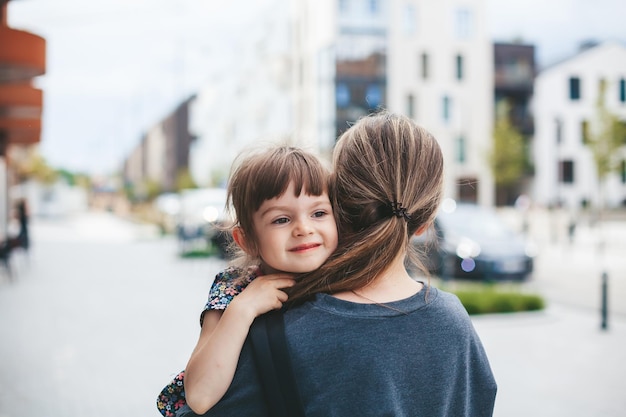 Young woman carrying her cute little daughter and they are hugging each other while walking on the street