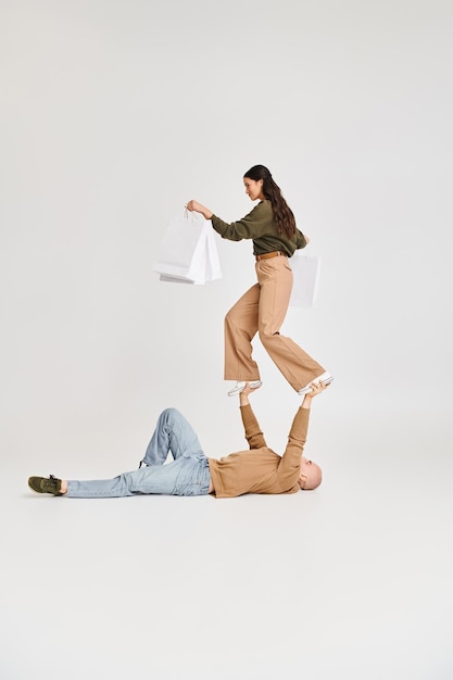 young woman in casual attire holding shopping bags and balancing of hands on strong man acrobats