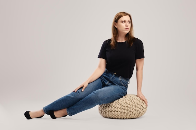 Young woman in casual black t shirt and jeans sits on the studio floor over grey background