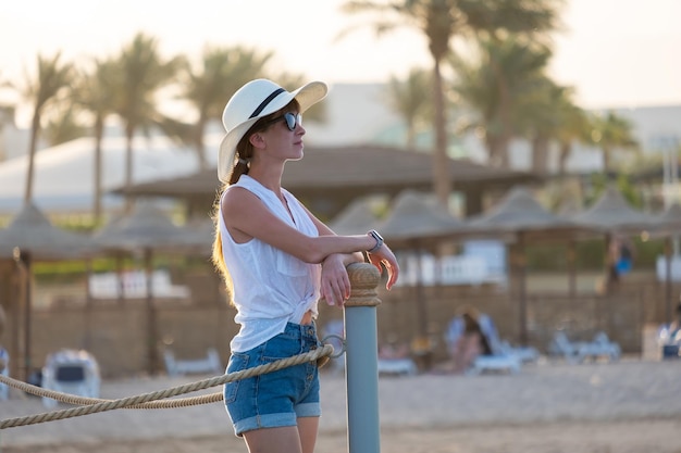 Young woman in casual outfit relaxing on seaside on warm evening. Summer vacations and travelling concept.