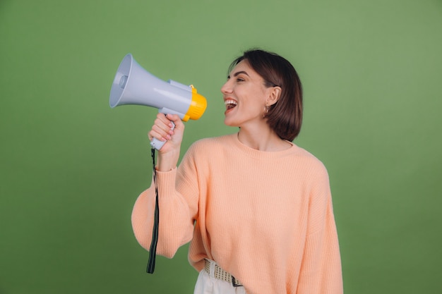 Young woman in casual peach sweater isolated on green olive color wall