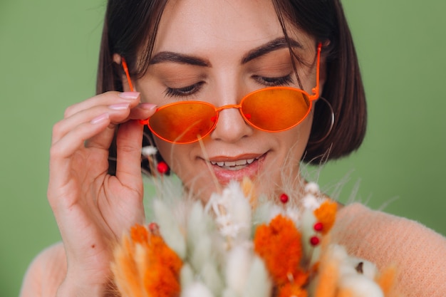 Young woman in casual peach sweater  isolated on green olive wall  hold  orange white flower box composition of cotton flowers, gypsophila, wheat and lagurus for a gift happy surprised