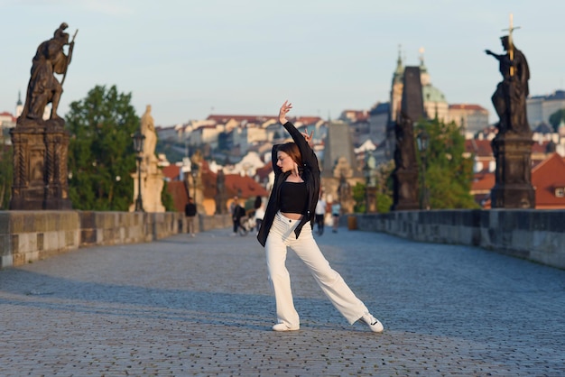 Young woman in casual stylish clothes dancing on the stone bridge of old town in a prague active