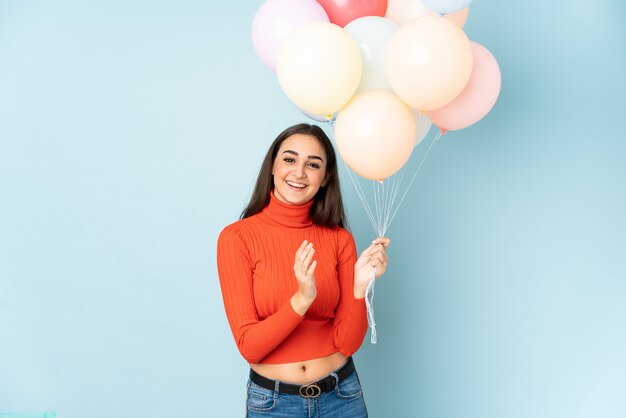 Young woman catching many balloons on blue applauding