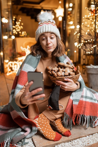 Young woman celebrating alone New Year holidays sitting with sweet gingerbreads on a terrace at home. Concept of quarantine and self-isolation during the epidemic on holidays