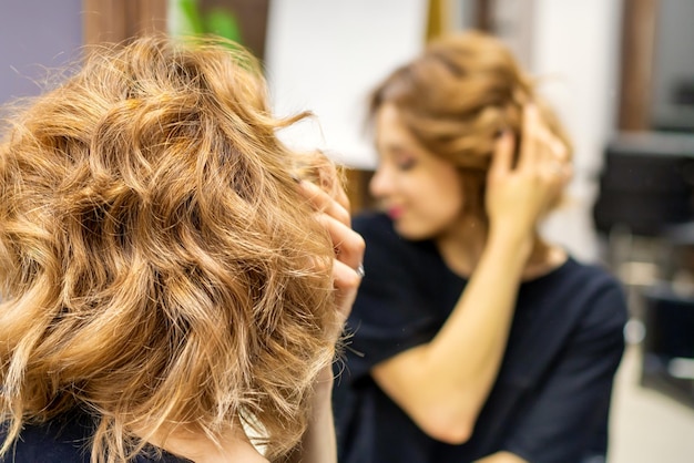 Young woman checking her new curly brown hairstyle in front of the mirror at the hairdresser salon