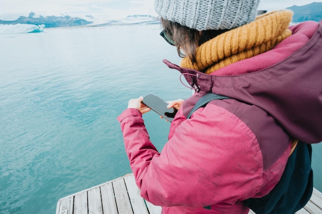 Young woman checking photos on smartphone at vatnajokull glacier having a fun day exploring Iceland