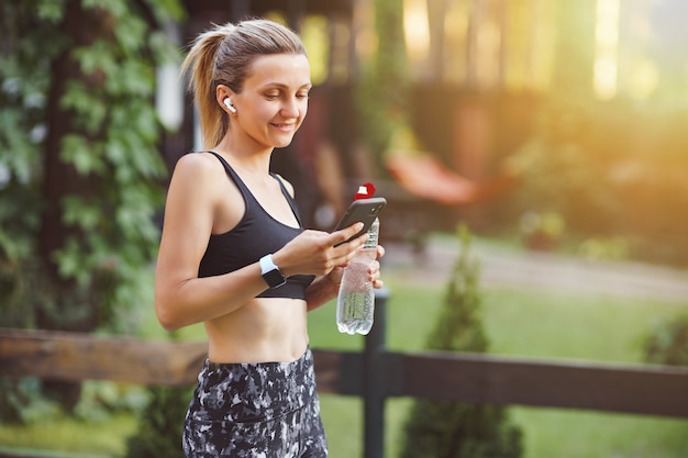 Young woman checking smart phone after workout on the green park wall.