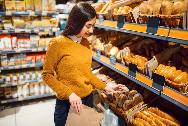 Young woman choosing bread in grocery store, bakery department