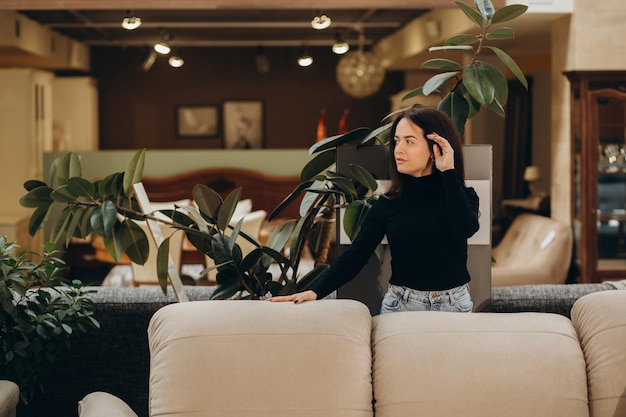 Young woman choosing sofa and pillow in furniture store