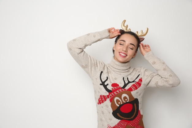 Young woman in Christmas sweater and deer headband on white background space for text