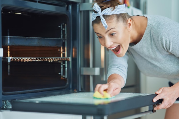 Young woman cleaning oven in the kitchen