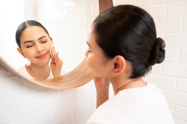 Young woman cleaning removing makeup on her face in bathroom at home beauty wellness concept