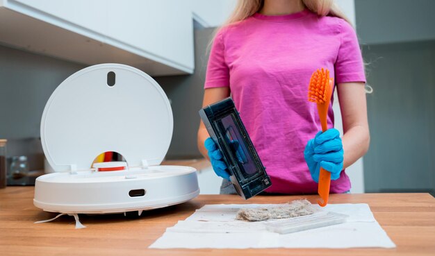 A young woman cleans a robot vacuum cleaner from dirt after cleaning