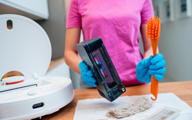 A young woman cleans a robot vacuum cleaner from dirt after cleaning