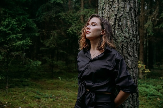 Photo young woman - close portrait in a dark forest. woman in black shirt