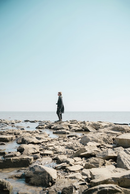 Young woman in a coat and scarft with camera standing on a deserted beach in cold weather