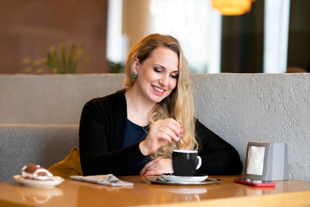 Young woman in a coffee shop drinks coffee in a shop happy female smiling and stirring cappuccino in...