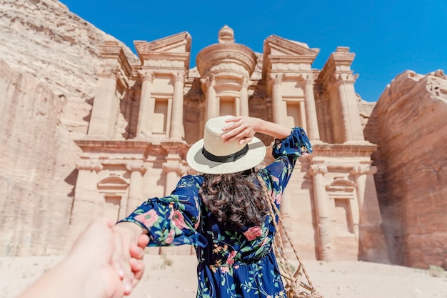 Young woman in colorful dress and hat holding man's hand and leading him to The Monastery