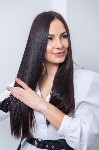 Young woman combing her long dark hair with a comb in a beauty salon.