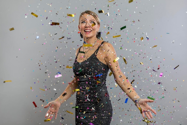 Young woman in confetti Laughing blonde in a smart black dress rejoices in a surprise on a holiday New Year's and Christmas Gray background