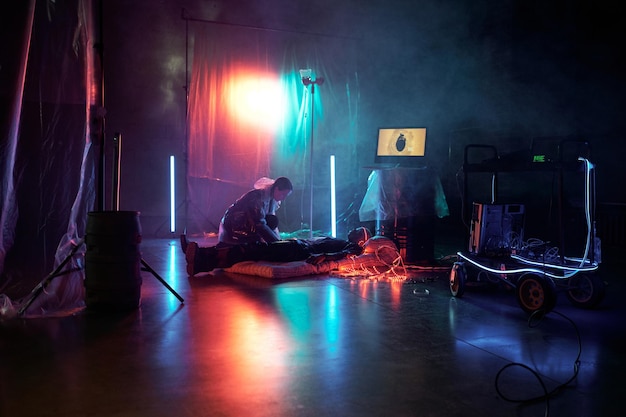 Young woman connecting man with virtual reality while he lying on mattress in dark room