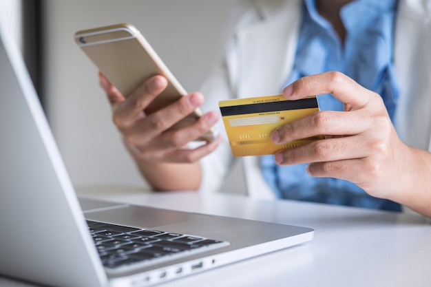 Young woman consumer holding smartphone, credit card and typing on laptop for online shopping and payment make a purchase on the Internet, Online payment, networking and buy product technology