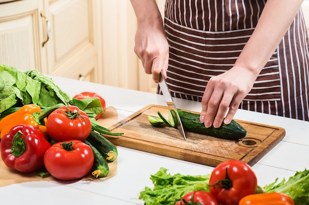 Young woman cooking in the kitchen at home. Healthy food. Diet. Dieting concept. Healthy lifestyle. Cooking at home. Prepare food. A woman cuts a cucumber and vegetables with a knife.